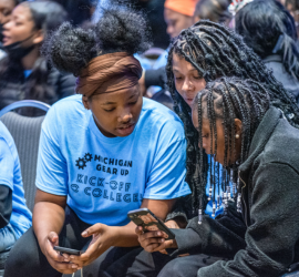 Three young people looking at a smartphone together, one wearing a light blue t-shirt with 