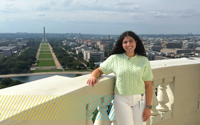 A person smiles while standing on a balcony overlooking the National Mall in Washington D.C., with the Washington Monument visible in the distance.