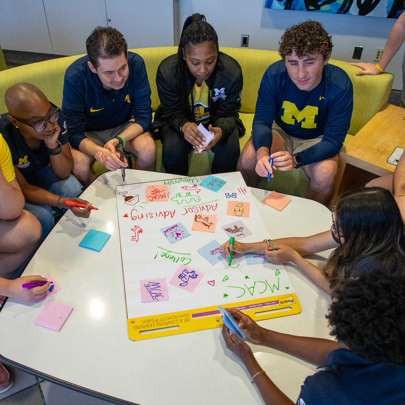students sitting on a couch in a circle around pieces of paper and markers