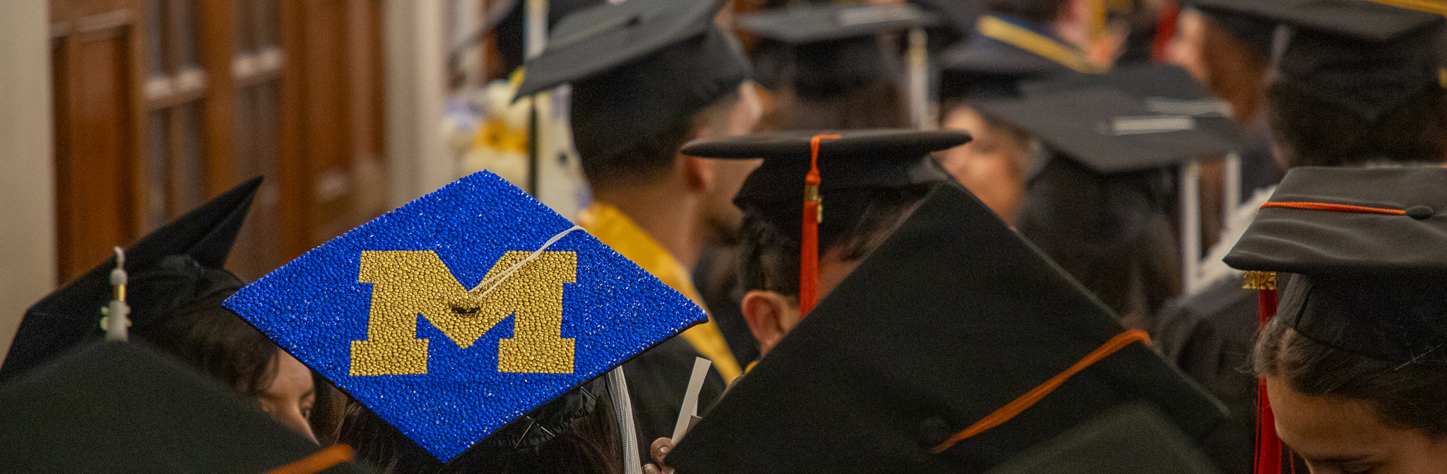 black graduation caps, with one sequined maize and blue cap with block M