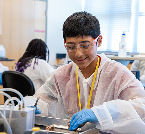 pre-teen boy wearing a white lab coat and blue gloves holding scissors over a tray